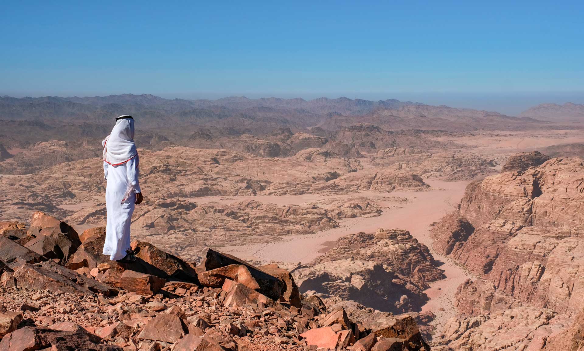 A bedouin standing in the summit Jabal Umm ad Dami, the highest mountain in Jordan. Panoramic landscape of the valleys and hills in the remote region of Jordan, near to the border with Saudi Arabia.