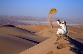 Man in traditional outfit in a desert at sunrise, throwing sand