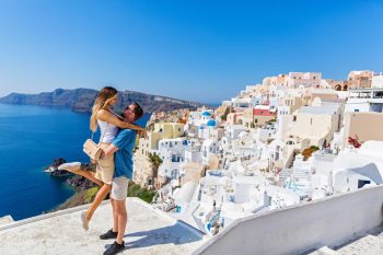 Young,Couple,Looks,Down,On,The,Landscape,Of,The,Island Young couple looks down on the landscape of the island of Santorini